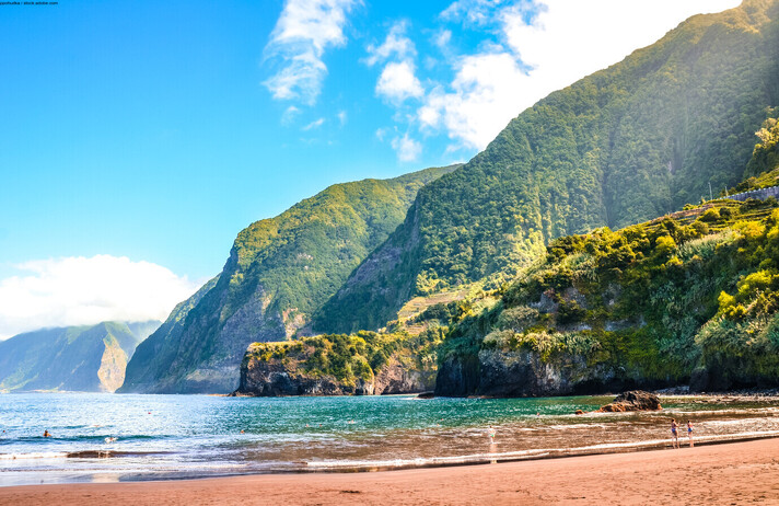 Beautiful sandy beach in Seixal, Madeira Island, Portugal. Green hills covered by tropical forest in the background. People on the beach. Summer vacation destination. Portuguese landscape.