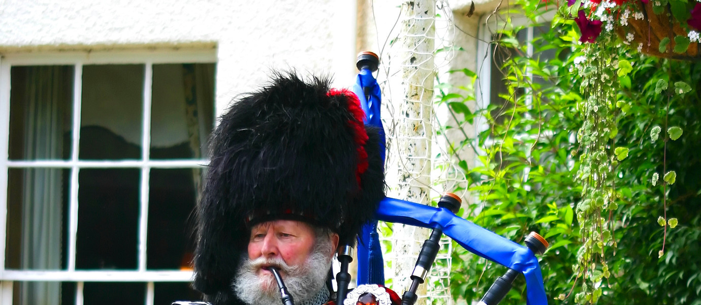 A Scottish bagpiper in full highland kilt dress and beard holding babpipes. Very colourful.