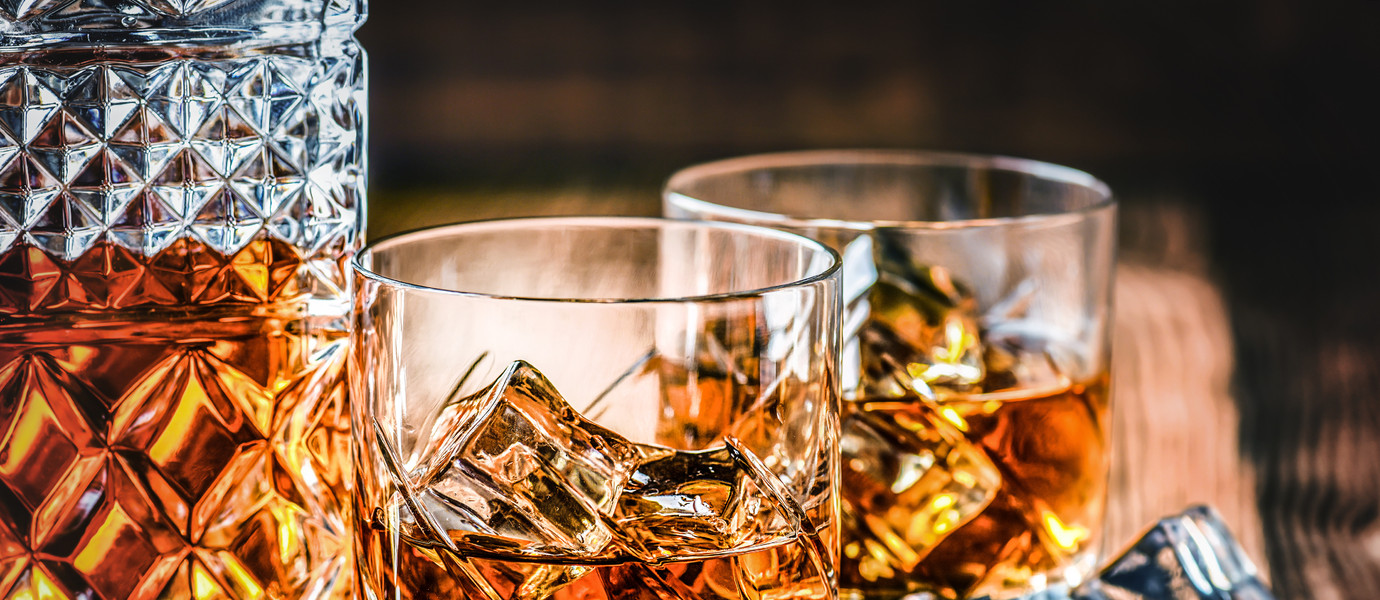 Glass of whiskey with ice cubes on black stone table. Side view with copy space alcohol concept.