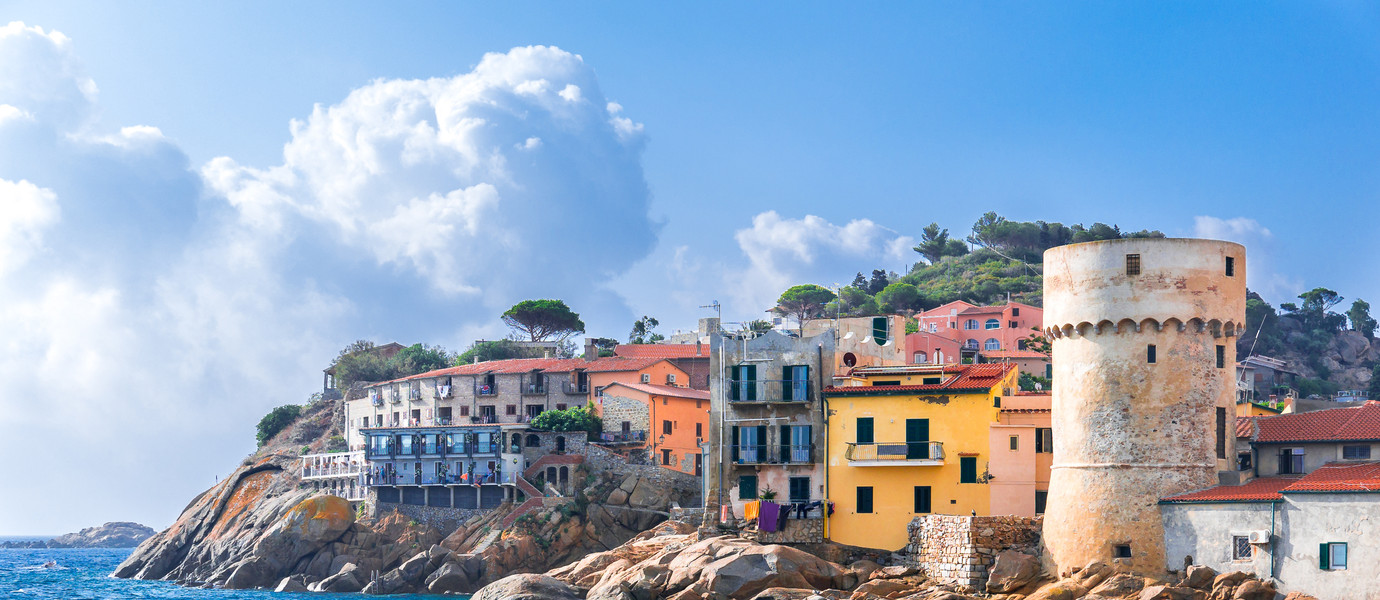 The perfect tiny seaside village of "Giglio Porto" with multi colored houses, an ancient defensive tower and a rocky coastline against a deep blue Mediterranean sea. - Giglio Island, Tuscany, Italy